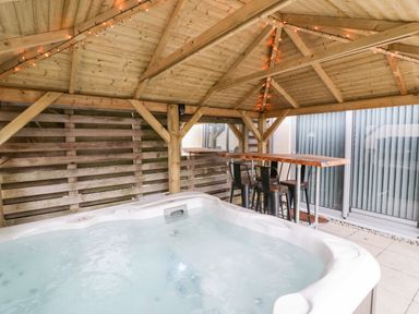 An outdoor covered area with a hot tub a bar table and chairs at Fistral Apres Surf in Newquay