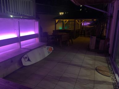 An outdoor patio area with wooden bench seating purple lighting a surfboard wooden table with chairs and a gazebo at Fistral Apres Surf in Newquay