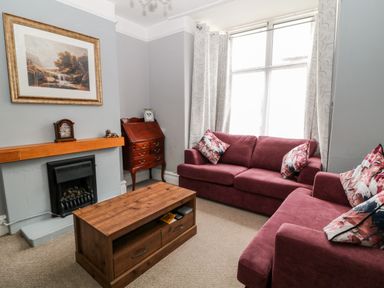 A living room with two red sofas floral cushions a wooden coffee table a fireplace and a wooden cabinet at Daisy Cottage in Bideford