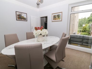 A dining room with a marble table and six chairs with a vase of flowers on the table and paintings on the walls at Daisy Cottage in Bideford