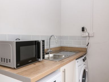 A kitchen countertop with a microwave, sink, and washing machine at Daisy Cottage in Bideford