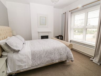 A bedroom with a double bed white bedding a chair a window with blinds and curtains and a fireplace at Daisy Cottage in Bideford