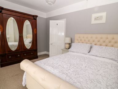 A bedroom with a cream upholstered bed a wooden wardrobe with mirrors a bedside table lamp and a framed picture on the wall at Daisy Cottage in Bideford
