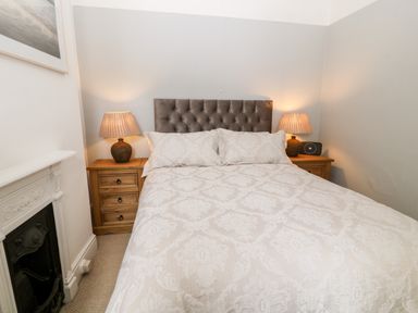 A bedroom with a double bed two bedside tables each with a lamp and a small fireplace at Daisy Cottage in Bideford