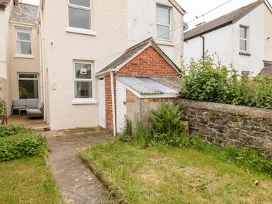 A backyard with a small brick and concrete outbuilding surrounded by grass and plants at Daisy Cottage in Bideford