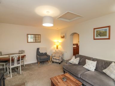 A living room with a gray sofa a wooden coffee table two armchairs a dining table with chairs and framed pictures on the walls at Chestnut Cottage in Filey