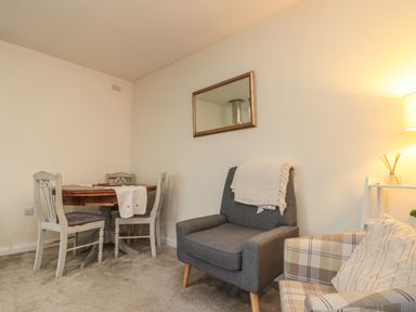 A room with a wooden dining table and three chairs a gray armchair with a blanket and a plaid armchair at Chestnut Cottage in Filey