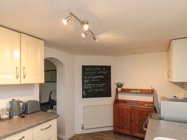 A kitchen with cream cabinets a wooden sideboard a microwave and a chalkboard with welcome message at Chestnut Cottage in Filey