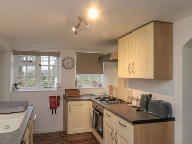 A kitchen with cream cabinets a gas stove a toaster a kettle and windows with blinds at Chestnut Cottage in Filey