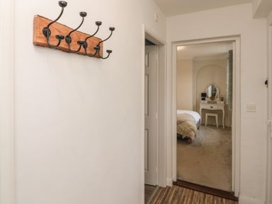 A hallway with a coat rack leading to a bedroom with a bed and a vanity table at Chestnut Cottage in Filey