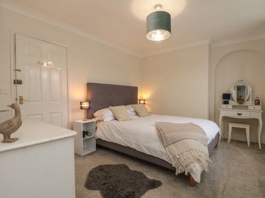 A bedroom with a double bed bedside tables a dressing table and a carpet at Chestnut Cottage in Filey