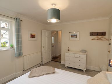 A bedroom with a bed a white chest of drawers two framed pictures a window with curtains and a coat rack at Chestnut Cottage in Filey
