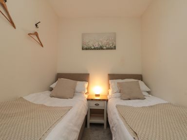 A bedroom with two single beds cushions and blankets a nightstand with a lamp and a painting on the wall at Chestnut Cottage in Filey