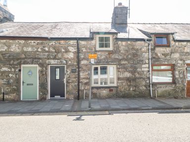 Stone cottage with three doors and three windows on a paved sidewalk at Weaver's Cottage in Tremadog