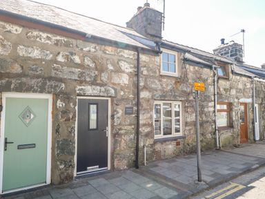 Stone exterior of a row of cottages with doors and windows on a street with a sign at Weavers Cottage in Tremadog
