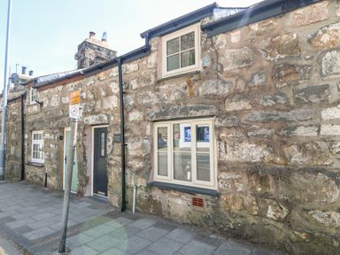 A stone cottage with two windows and two doors beside a sidewalk with a street sign at Weavers Cottage in Tremadog