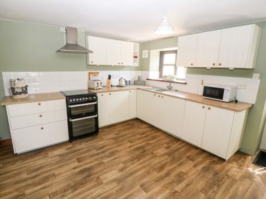 A kitchen with white cabinets wooden countertops a black stove a microwave a toaster and a coffee machine at Weavers Cottage in Tremadog