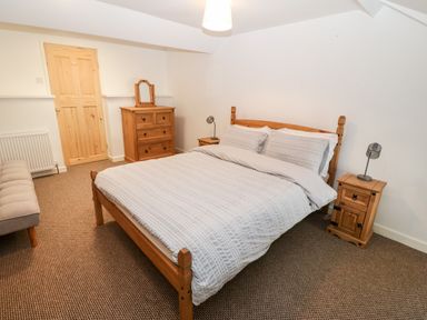 A bedroom with a wooden bed frame a chest of drawers and bedside tables with lamps at Weavers Cottage in Tremadog