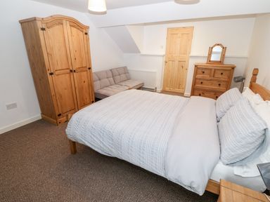 A bedroom with a bed sofa wardrobe dresser and a wooden door at Weavers Cottage Tremadog