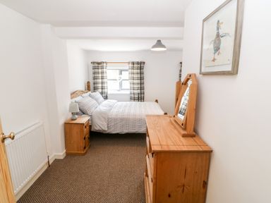 A bedroom with a bed bedside table and chest of drawers with a mirror at Weaver's Cottage in Tremadog