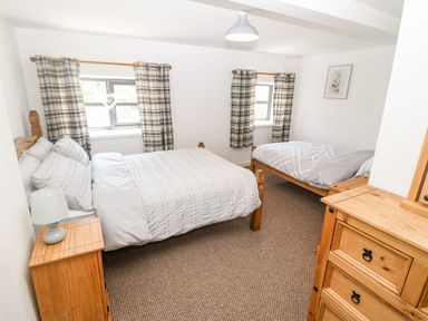 A bedroom with two wooden beds two windows with plaid curtains and wooden furniture at Weavers Cottage in Tremadog