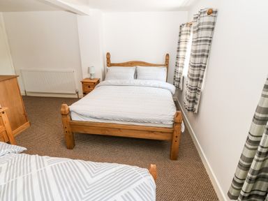 A bedroom with two wooden beds a wooden chest of drawers and a nightstand with a lamp at Weavers Cottage in Tremadog