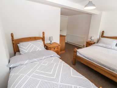 A bedroom with two wooden beds a chest of drawers and bedside tables with lamps at Weavers Cottage in Tremadog