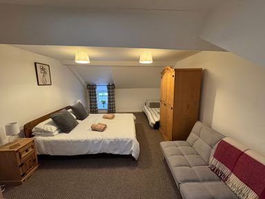A bedroom with two beds a wardrobe a sofa and a bedside table at Weavers Cottage in Tremadog