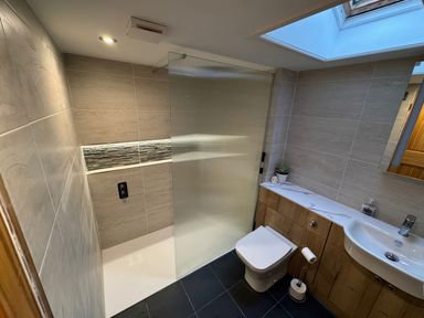 A bathroom with a walk in shower separated by a glass panel with a toilet and a sink with wooden cabinets underneath at Weavers Cottage in Tremadog