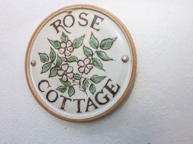 A round ceramic sign with flowers and leaves on a wall at Rose Cottage in Marldon