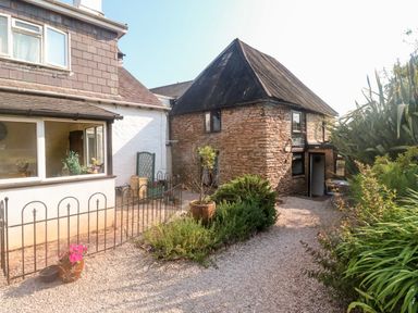 A gravel pathway with plants and a flower pot beside a stone building with a thatched roof at Rose Cottage in Marldon