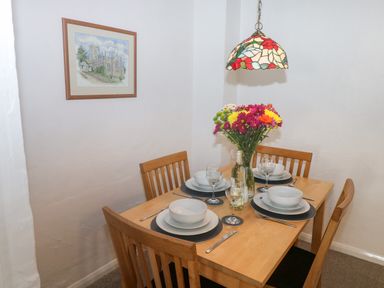 A dining area with a wooden table set for four with plates bowls glasses utensils a vase of flowers and a stained glass hanging lamp at Rose Cottage in Marldon
