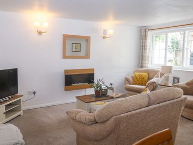 A living room with beige sofas a coffee table a wall-mounted fireplace and a television at Rose Cottage in Marldon