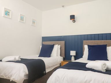 A bedroom with two single beds with blue pillows and blankets and a nightstand with a lamp at Rose Cottage in Marldon