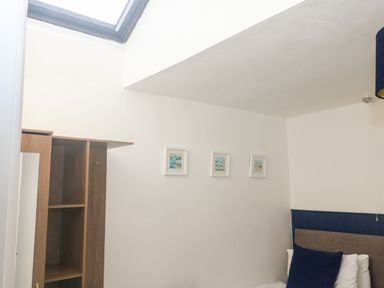 A bedroom corner with three small framed pictures on a white wall a wooden shelving unit and a bed with white pillows and a navy blue cushion at Rose Cottage in Marldon