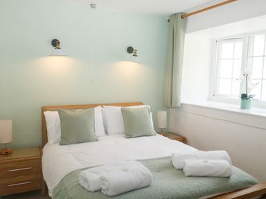 A bedroom with a double bed two nightstands two wall lamps and a window with curtains at Rose Cottage in Marldon