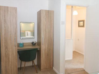 A bedroom corner with a wooden desk and two wardrobes with a green chair and a mirror at Rose Cottage in Marldon
