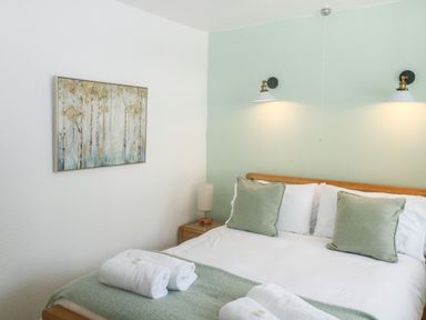 A bedroom with a bed with pillows and towels on it a bedside table with a lamp and wall lights above the bed at Rose Cottage in Marldon
