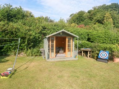 A wooden garden shed with double doors open on a lawn with bushes and trees in the background at Rose Cottage in Marldon