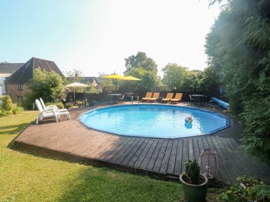 An outdoor octagonal swimming pool with chairs tables and umbrellas on a wooden deck in a garden at Rose Cottage in Marldon