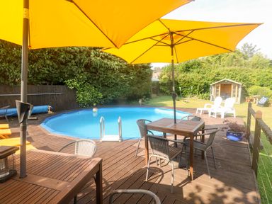 An outdoor area with a swimming pool surrounded by wooden decking and yellow umbrellas at Rose Cottage in Marldon