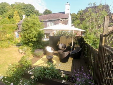 An outdoor seating area with four chairs and a table under a large umbrella on a deck surrounded by plants and flowers at Rose Cottage in Marldon
