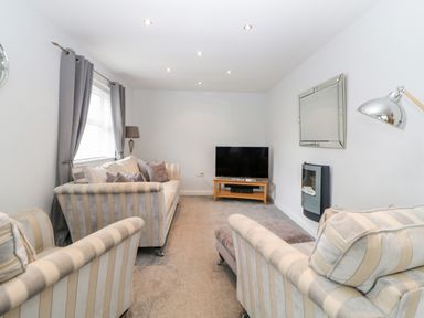 A living room with striped sofas a television on a wooden stand and a wall-mounted fireplace at Fonthill in Torquay