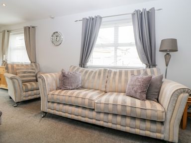 A living room with a striped sofa and armchair under windows with gray curtains at Fonthill in Torquay