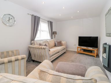 A living room with striped sofas a flat screen tv on a wooden stand and a wall clock at Fonthill in Torquay