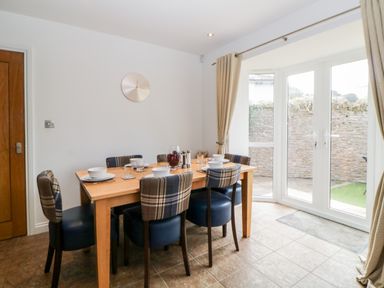 A dining area with a wooden table and six chairs next to glass doors leading outside at Fonthill in Torquay