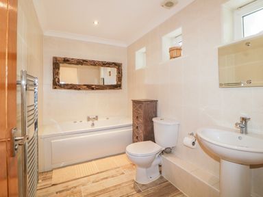 A bathroom with a bathtub a toilet a sink a large mirror and a wooden cabinet at Fonthill in Torquay