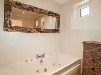 A bathroom with a rectangular bathtub a wooden framed mirror and a wooden chest of drawers at Fonthill in Torquay