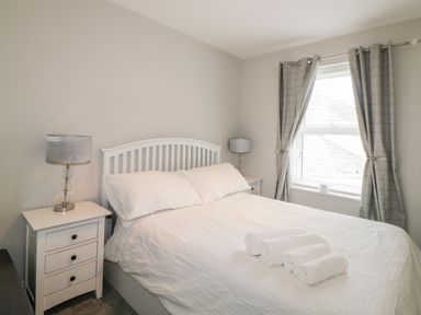 A bedroom with a double bed with white bedding and rolled towels on top with two bedside tables and lamps by a window with curtains at Fonthill in Torquay