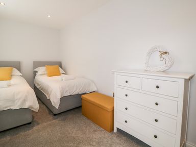 A bedroom with two single beds a white dresser and a mustard storage bench at Fonthill in Torquay